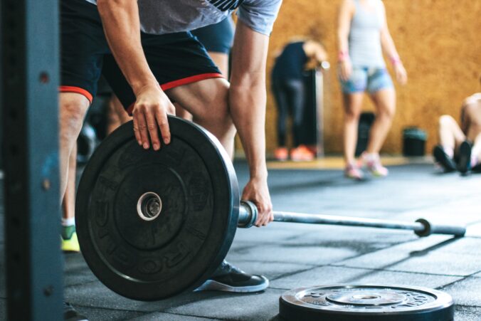 Bilden visar en person som tränar på ett gymgolv och plockar på bumpers på skivstång. Det är viktigt att välja ett slitstarkt gymgolv vid funktionell träning och styrketräning.